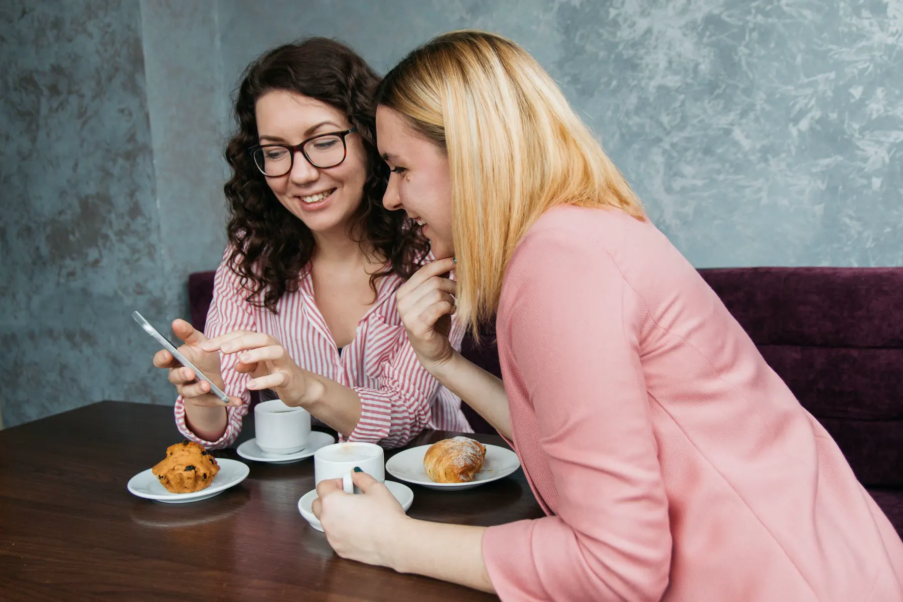Twee vriendinnen lachen bij koffie en gebak in een café