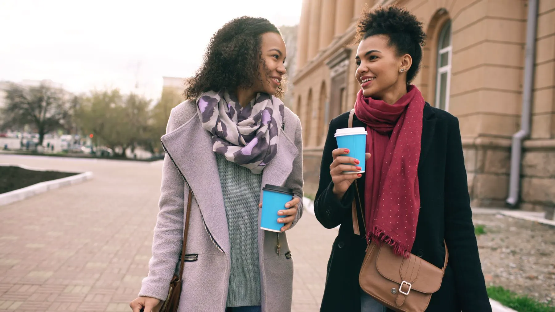 Twee vrouwen wandelen lachend met een koffiebekertje over straat