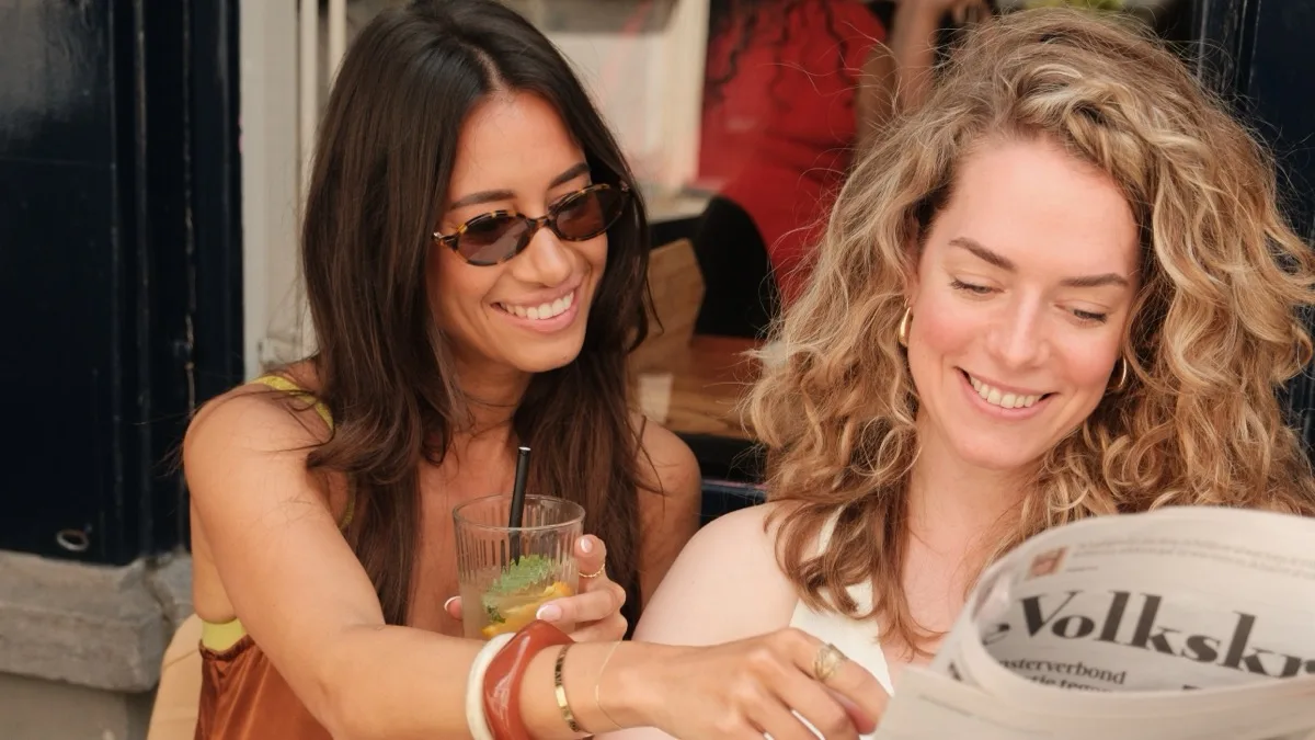 Twee vrouwen lezen lachend samen de krant op een terras